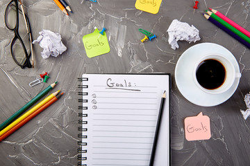 Goals as memo on notebook with idea, crumpled paper, cup of coffee over on grey background. Top view.