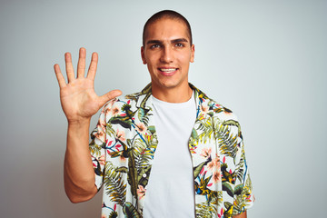 Poster - Young handsome man on holidays wearing Hawaiian shirt over white background showing and pointing up with fingers number five while smiling confident and happy.