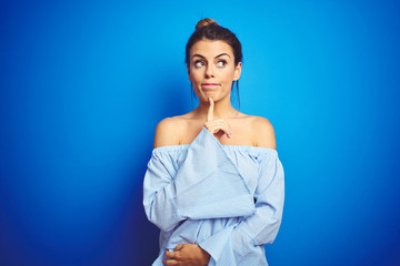 Canvas Print - Young beautiful woman wearing bun hairstyle over blue isolated background Thinking concentrated about doubt with finger on chin and looking up wondering