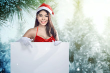 Asian Woman In Santa Costume Holding A White Board With Snowy Fir Trees Background