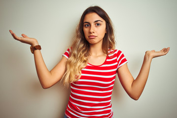 Canvas Print - Young beautiful woman wearing red stripes t-shirt over white isolated background clueless and confused expression with arms and hands raised. Doubt concept.