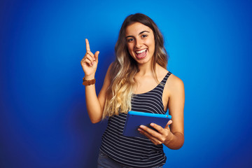 Poster - Young beautiful woman using touchpad tablet over blue isolated background very happy pointing with hand and finger to the side