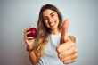 © Krakenimages.com - Young beautiful woman eating red apple over grey isolated background happy with big smile doing ok sign, thumb up with fingers, excellent sign