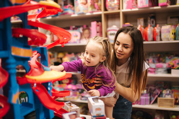 Adorable little girl with mother shopping for toys. Cute female in toy store. Happy young girl selecting toy with her mom