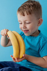 Wall Mural - Little Boy Holding and eating an Banana on blue background, food, diet and healthy eating concept