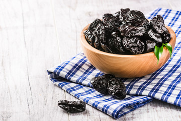 Wall Mural - Fresh dried prunes in wood bowl on blue cloth and white old rustic table. Dried plums on table. Fresh prunes for perfect health.