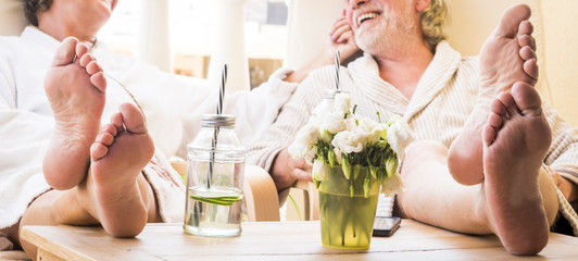 close up of feet of couple of seniors on the tale in a resort hotel or at home with a cocktail or drink - healthy and great lifestyle - enjoying together sitted at home