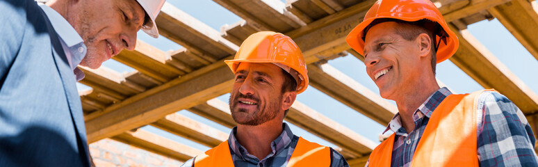 panoramic shot of builders near mature businessman in helmet