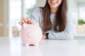 Young woman smiling putting a coin inside piggy bank as savings for investment