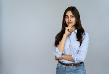 Wall Mural - Thoughtful serious doubtful young indian adult woman standing isolated on grey studio background with copy space. Pondering lady student professional thinking of new idea looking at camera, portrait