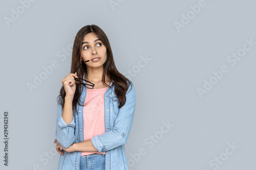 Fotomural Curious young adult indian woman standing isolated on grey background with copy space