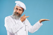 © Seventyfour - Waist up portrait of charismatic bearded chef pointing at copy space standing against blue background, mock up template
