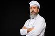 © Seventyfour - Professional waist up portrait of bearded senior chef posing against black background standing with arms crossed, copy space