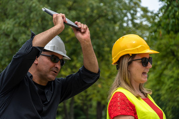 Conflict and disagreement at work on construction site. Angry construction boss yelling at an architect threatening to hit her with a digital tablet