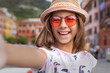 © studio GDB - Cute and carefree child girl is making selfie with smartphone while traveling at Cinque Terre, Italy.