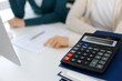© Iryna - Calculator and binders with papers are waiting to be processed by business woman or bookkeeper working at the desk in office back in blur. Internal Audit and tax concept