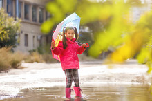 Adorable Little Girl Holding White Umbrella Standing In A Puddle On Warm Autumn Day