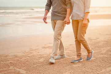 Wall Mural - Senior lovers walk hand in hand at the beach at sunset, plan life insurance at retirement concept.