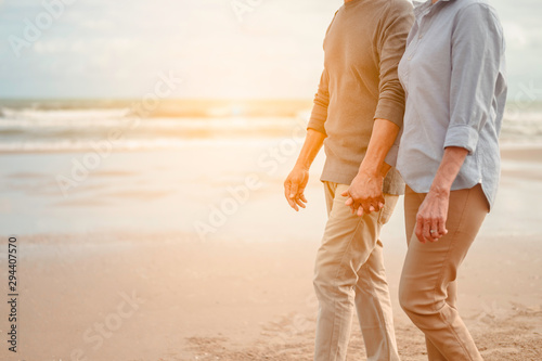 Fotomural Senior lovers walk hand in hand at the beach at sunset, plan life insurance at retirement concept