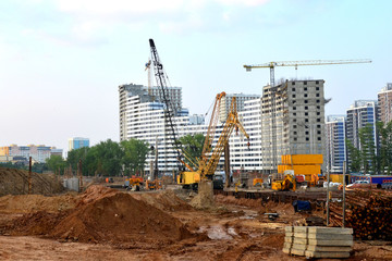 Wall Mural - Huge construction site with a lot of construction equipment, houses under construction, tower cranes and workers. Piles driven into the ground by hydraulic hammering. Subway construction project