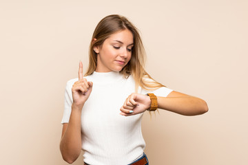 Young blonde woman over isolated background looking at the hand watch