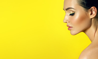 Face in profile close-up on a yellow background of a beautiful young girl with perfect smooth skin and bright eye make-up.