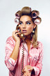 © EkaterinaJurkova - A beautiful young showy girl with bright pin-up make-up speaks on a golden dial telephone in pink striped silk pajamas and pink curlers.