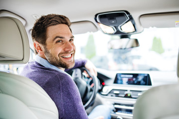 Businessman sitting in brand new car, looking back when driving.