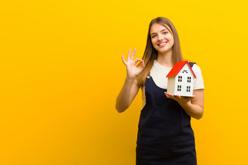 young pretty woman with a house model against orange background