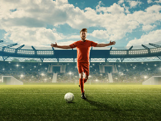 Wall Mural - Professional soccer player in sports uniform with a ball on a field with tribunes, green grass and spectators. Blue cloudy sky