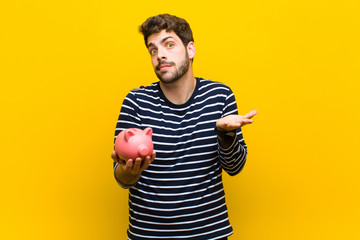 young handsome man holding a piggy bank against orange backgroun