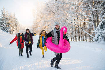 A group of young friends on a walk outdoors in snow in winter forest.