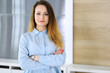 © Iryna - Business woman headshot at workplace in modern office. Unknown businesswoman standing straight with arms crossed. Young accountant or secretary looks good