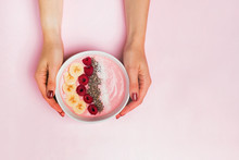 Woman's hands holding smoothie bowl with raspberries on pink background