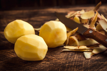 Peeling potatoes. Peel raw potatoes and potatoes on an old wooden Board and knife.