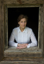Portrait Of Woman Looking Out Of Window Of An Old Wooden House