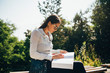 © Westend61 - Young woman sitting on a bench in a park looking at an open book