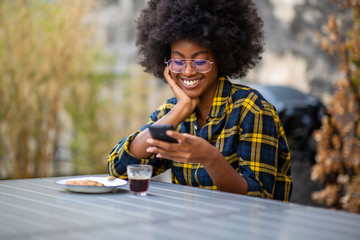 Wall Mural - young african American woman smiling outside looking at mobile phone