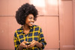 © mimagephotos - cheerful young black woman holding mobile phone and looking away