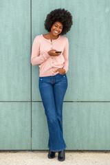 Poster - Full body happy smiling young woman leaning against green wall and looking at mobile phone