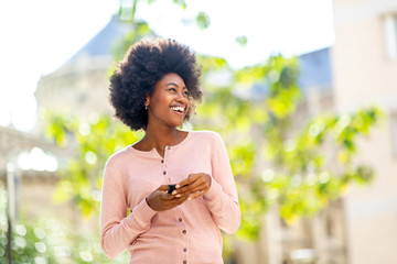 Wall Mural - laughing young african american girl with cellphone outside in city