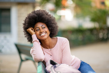 Poster - happy beautiful young african american woman with afro sitting outside on park bench