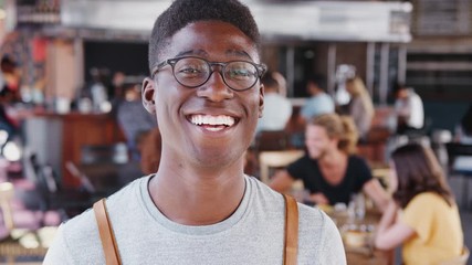 Wall Mural - Portrait Of Waiter In Busy Bar Restaurant Smiling At Camera