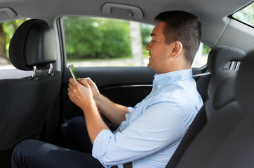 Wall Mural - transport, business and communication concept - male passenger or businessman using smartphone on back seat of taxi car