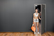 Sexy athletic girl enters the gym. Sportswoman opens the door to the locker room. Stylish black interior of modern fitness gym. Concept of health. European brunette girl holding a sports bag..