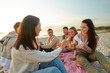 © Syda Productions - friendship, leisure and fast food concept - group of happy friends eating sandwiches or burgers at picnic on beach in summer