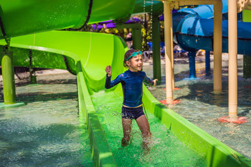 Wall Mural - Happy boy on water slide in a swimming pool having fun during summer vacation in a beautiful tropical resort