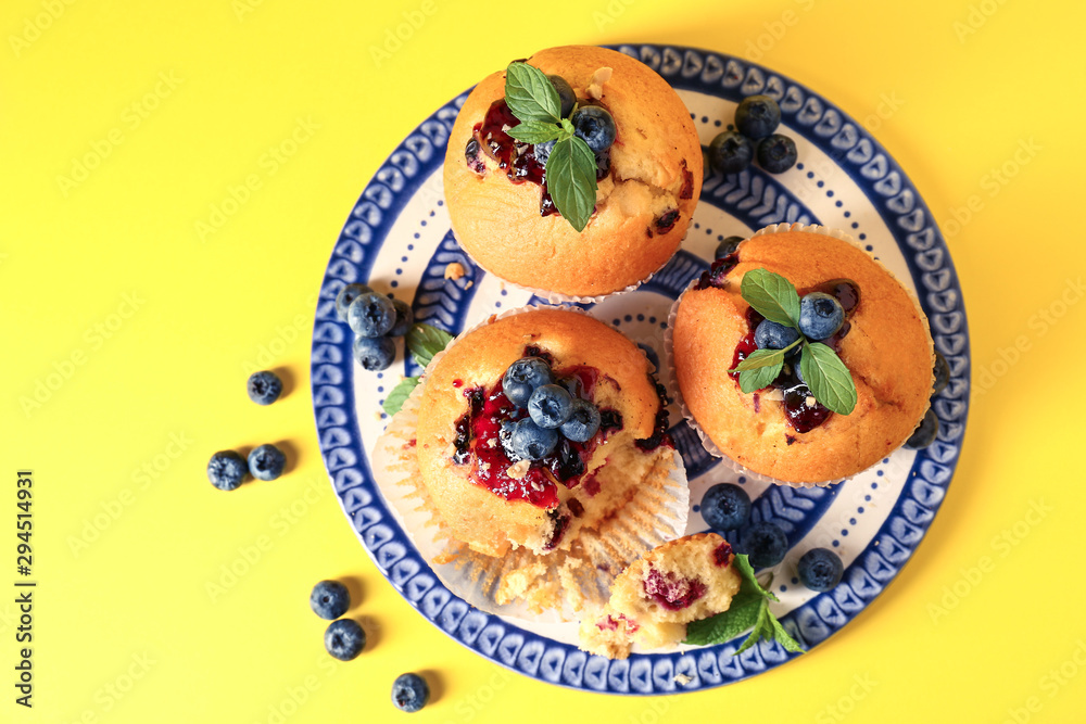 Plate with tasty blueberry muffins on color background