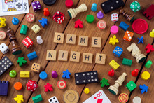 "Game Night" Spelled Out In Wooden Letter Tiles, Surrounded By Dice, Cards, Dominoes, Chess Pieces And Other Game Pieces On A Wooden Background