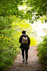 Wall Mural - blond woman in dark hiking clothes and pink backpack walking in forest in autumn in park, Seen from behind, telephoto lens. Gatineau Park, Quebec, Ontario.